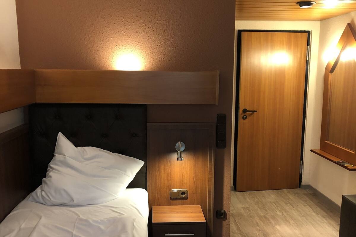 Une chambre d’hôtel avec un lit, une table de chevet, une porte en bois et une petite étagère.