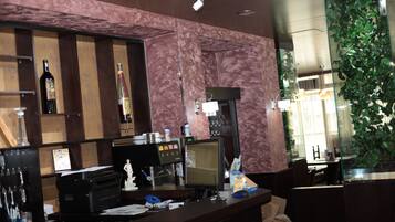 Una zona de bar con pared de mármol, un monitor de computadora, una caja registradora y varias botellas.
