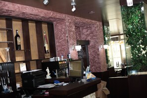 Una zona de bar con pared de mármol, un monitor de computadora, una caja registradora y varias botellas.