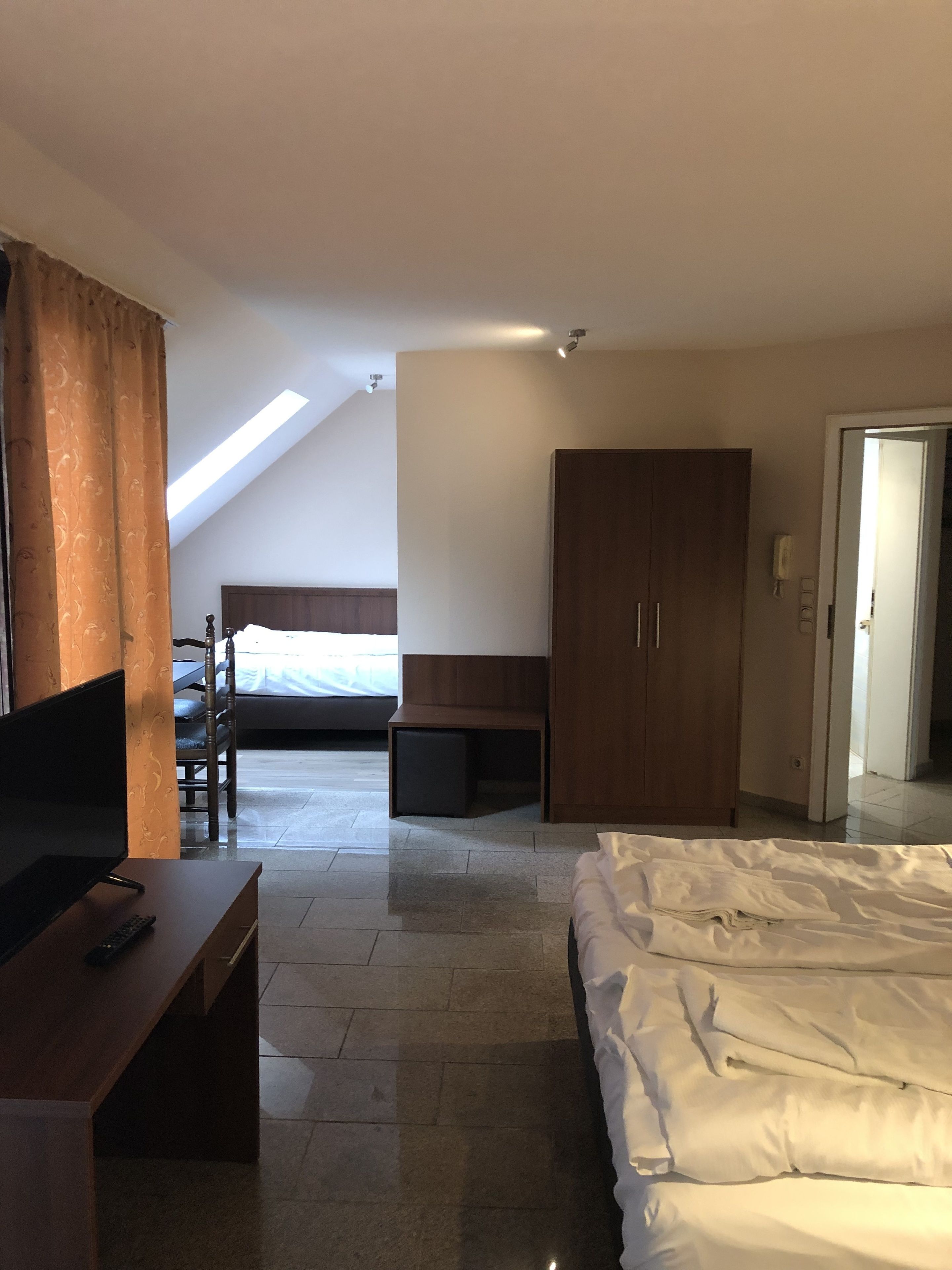 A modern hotel room with a bed, a desk, a wardrobe, and a TV.