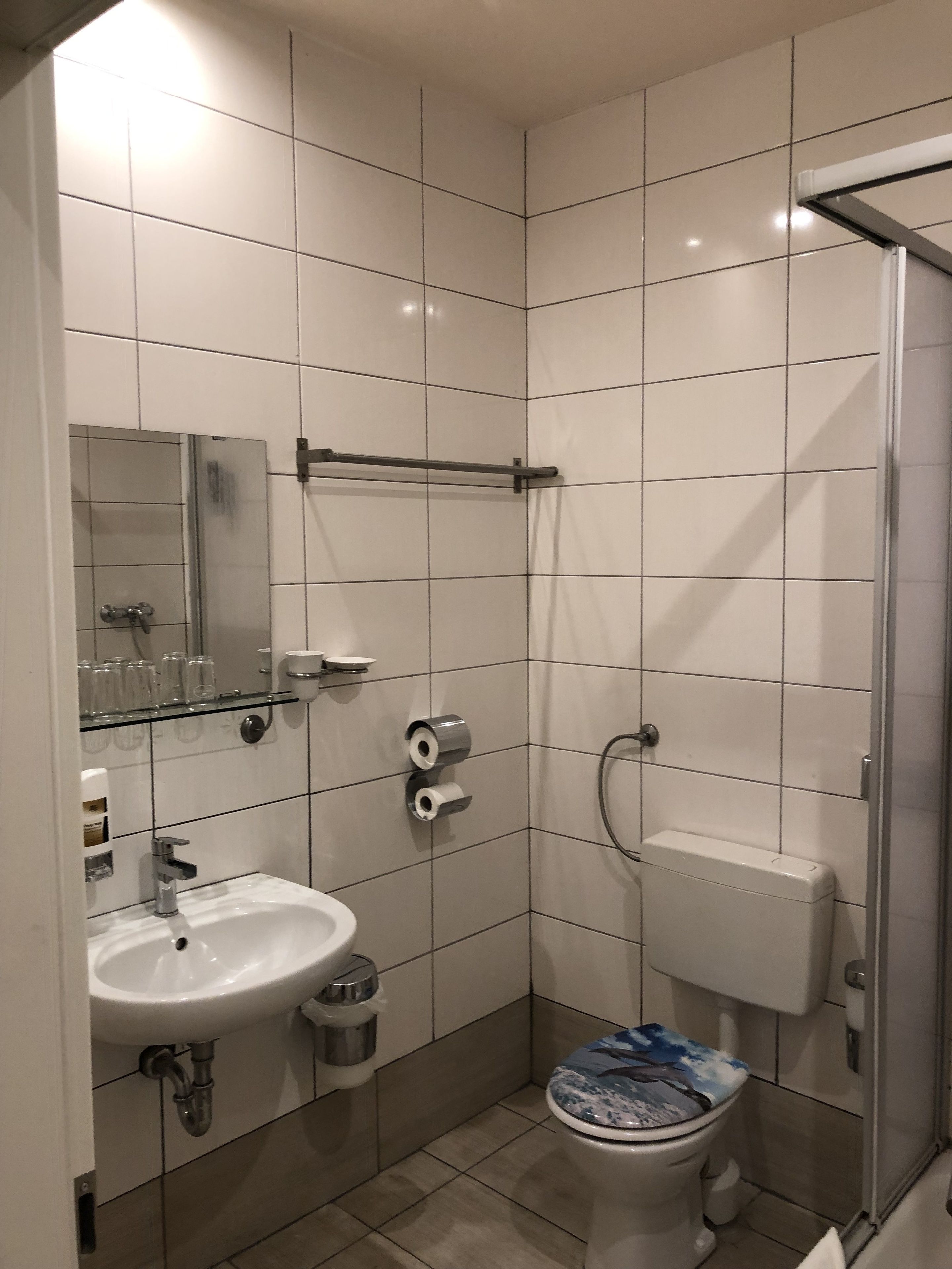 A bathroom with white tiles, a sink, a toilet, and a shower.