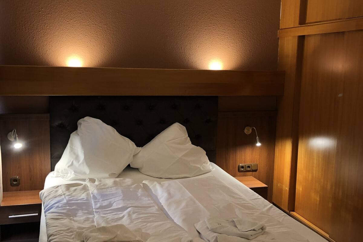Un lit bien fait, avec du linge de lit blanc, une tête de lit capitonnée et des lampes de chevet.