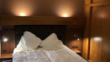 Una cama bien hecha con sábanas blancas, un cabecero acolchado y lámparas de noche.