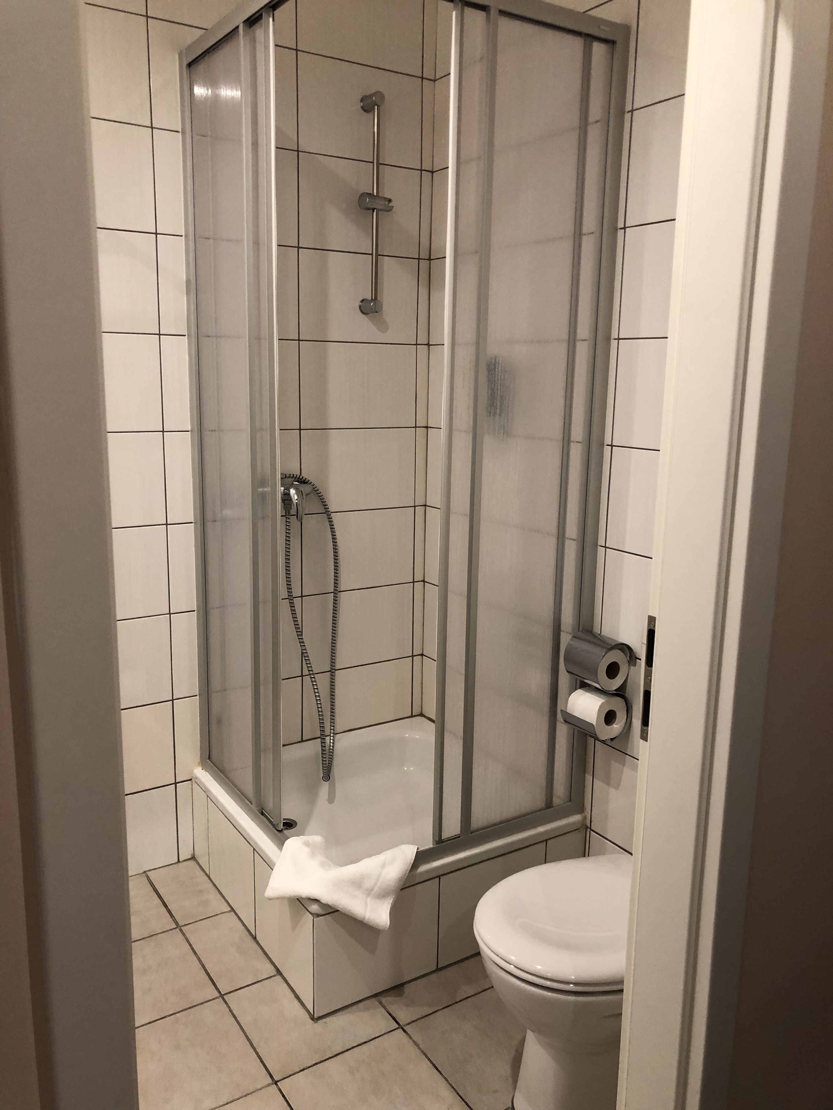 Eine Duschkabine mit Glastür, einer Handbrause und einem Handtuchhalter.