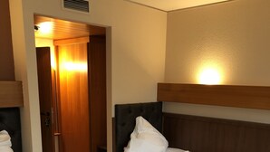 A hotel room with two single beds, wooden headboards, and a wooden door with a light above it. - Hotel & Restaurant Poseidon (Bayreuth)