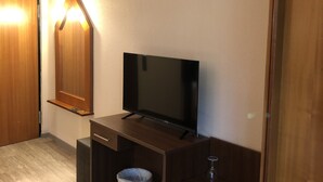 A small room with a wooden desk, a television, a trash bin, and a door. - Hotel & Restaurant Poseidon (Bayreuth)