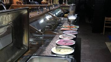 Montaje de bufé con diversos alimentos y una zona de bar con botellas y vasos.
