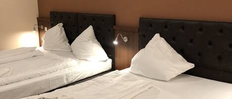 A hotel room with two beds, each with a dark headboard and white bedding.