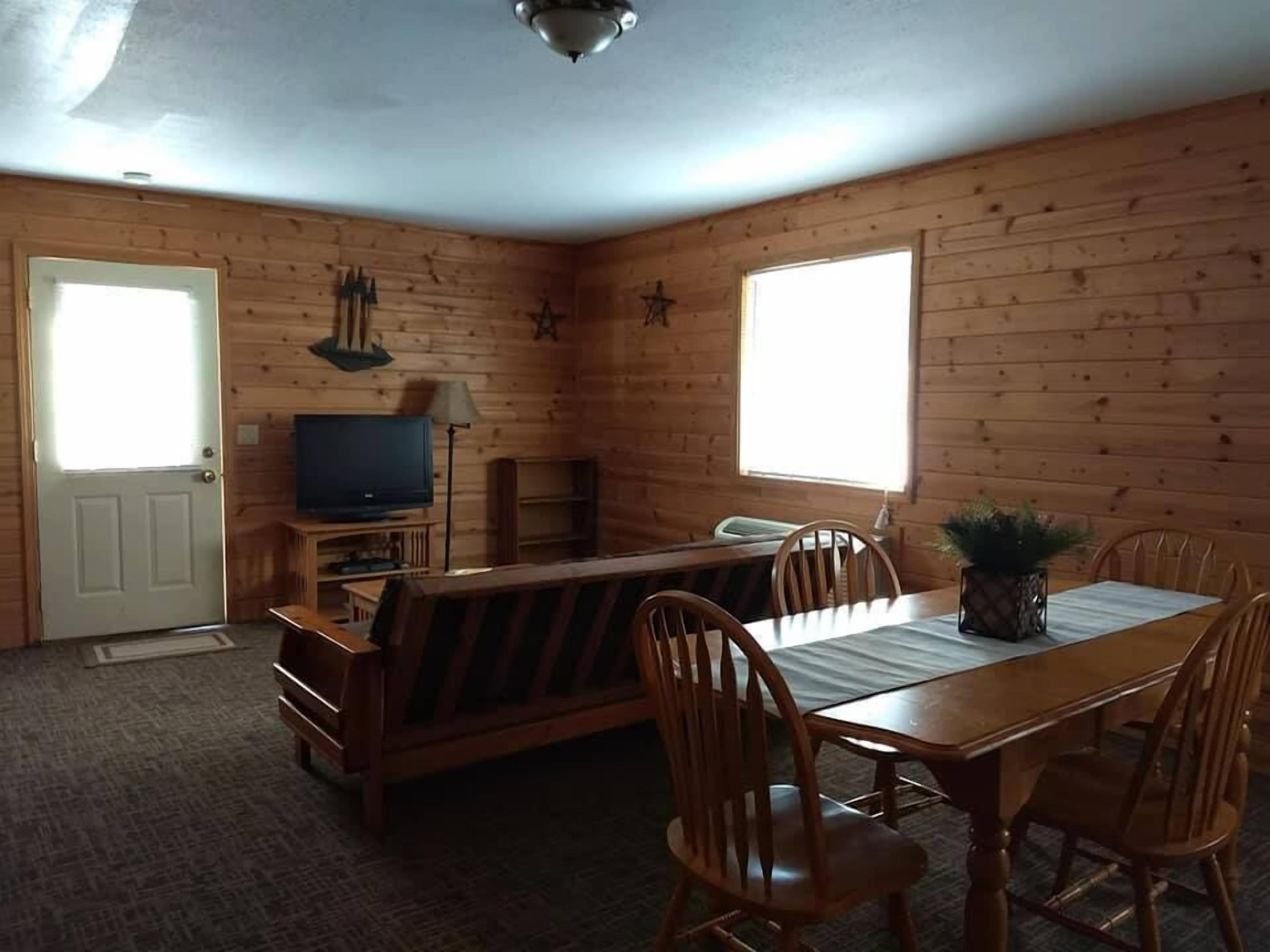 Un intérieur en bois comprenant une table à manger, des chaises, un téléviseur et une petite kitchenette.