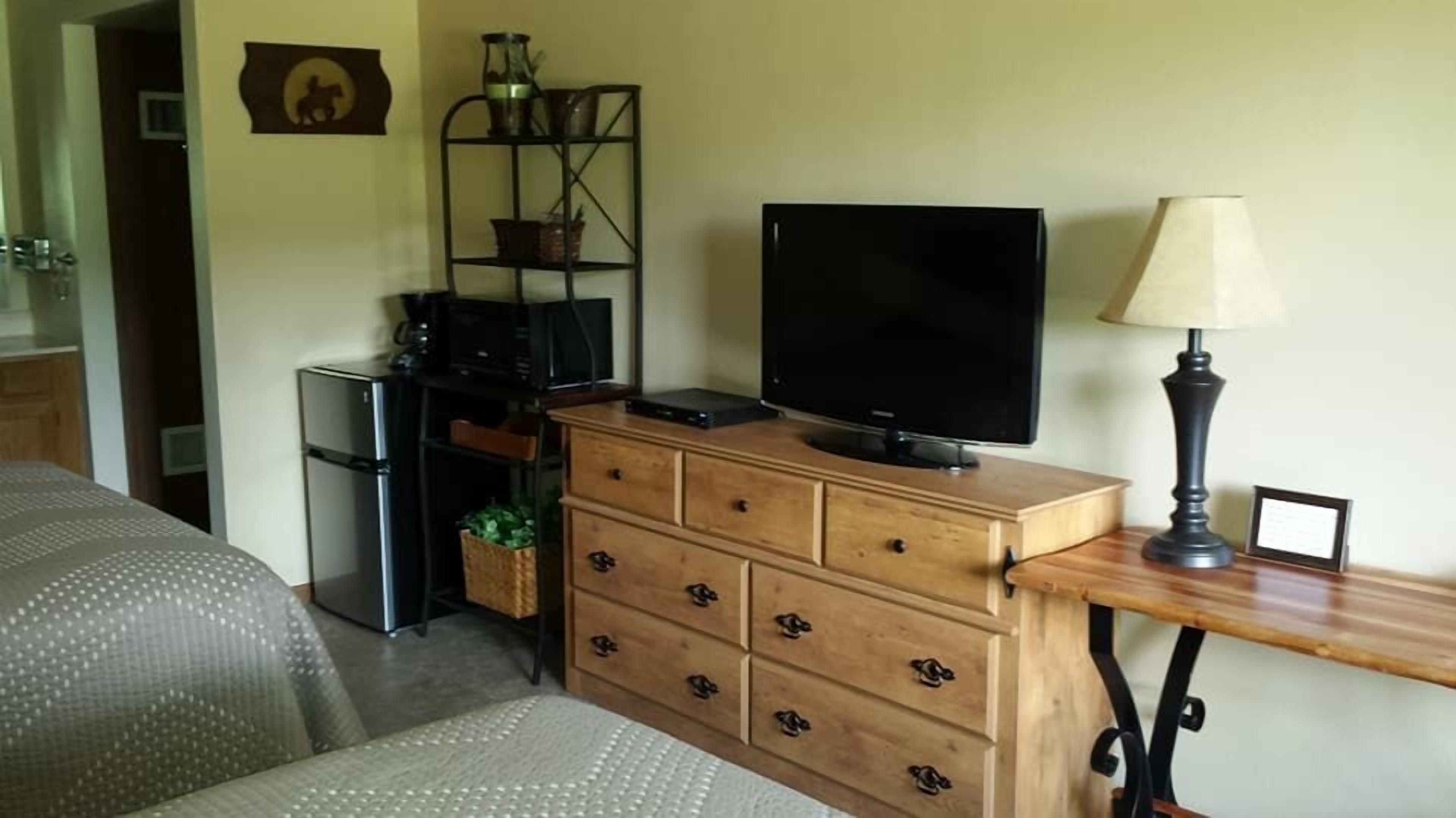 Ein kleiner Wohnraum mit einem Holzkasten, einem Fernseher, einer Lampe und einer Mikrowelle.