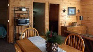 A wooden cabin interior with a dining table, chairs, a microwave, and a fireplace.