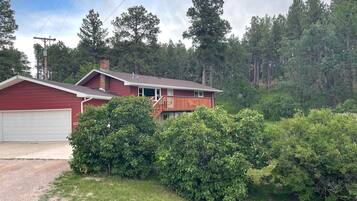 Une maison rouge avec une porte de garage blanche, entourée d’arbustes et d’arbres aux feuillages denses et verdoyants.
