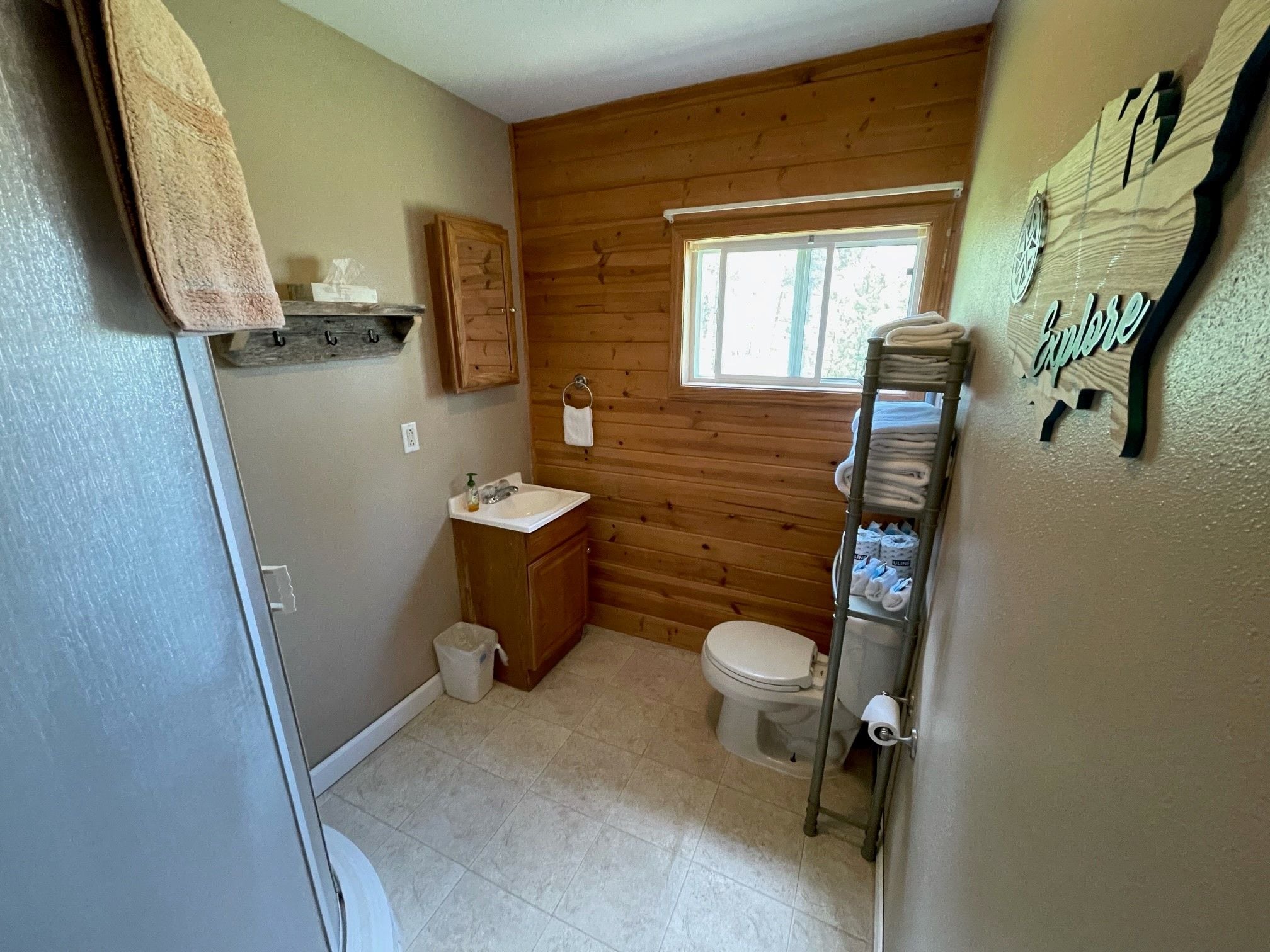 A compact bathroom with a wooden wall, a window, a sink, and a toilet.