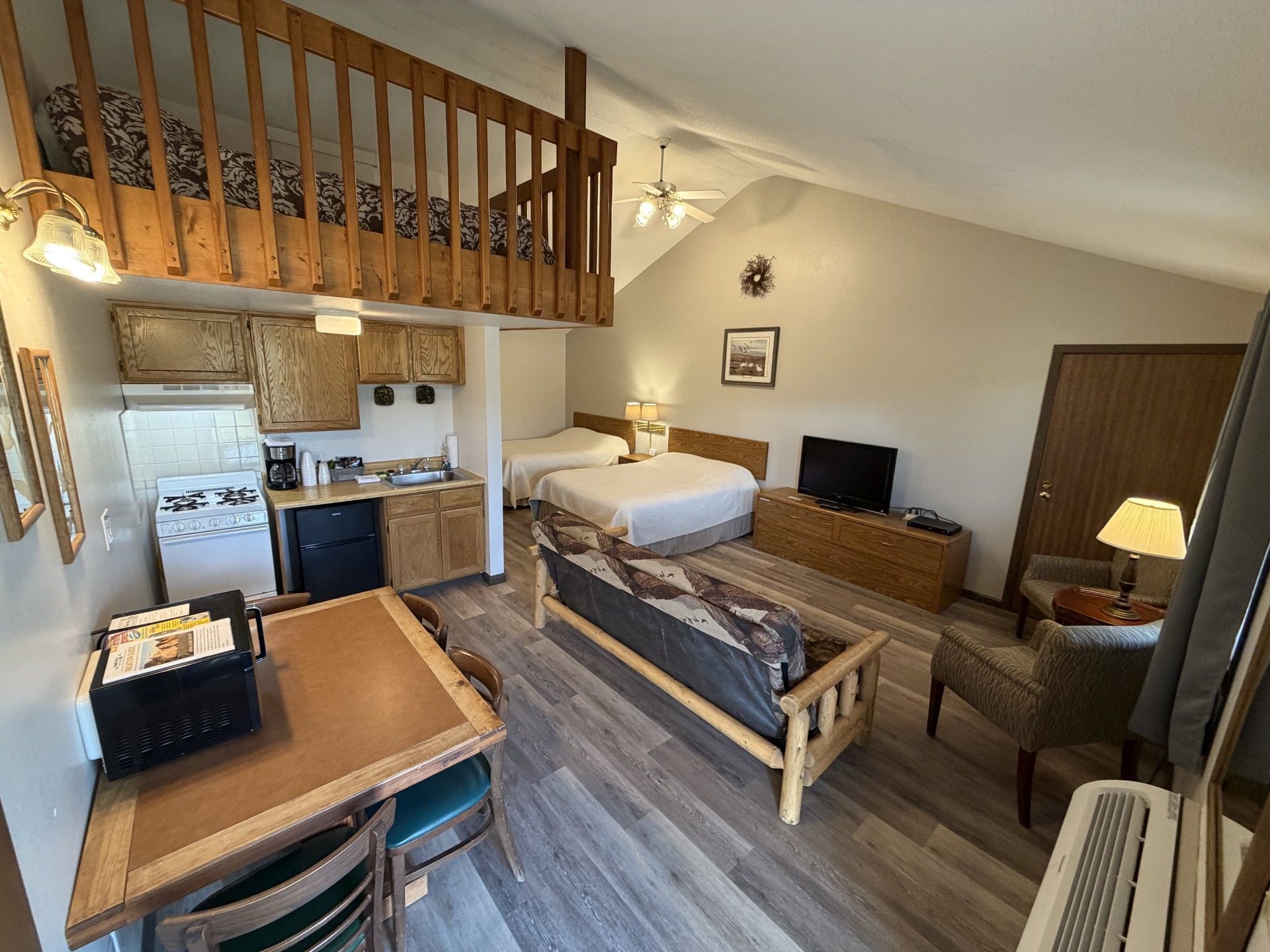 Une pièce compacte comprenant un lit en mezzanine, un coin cuisine, un espace repas et un lit simple.