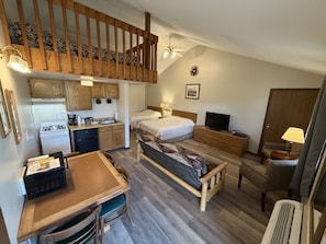 A compact room with a loft bed, a kitchenette, a dining area, and a single bed.