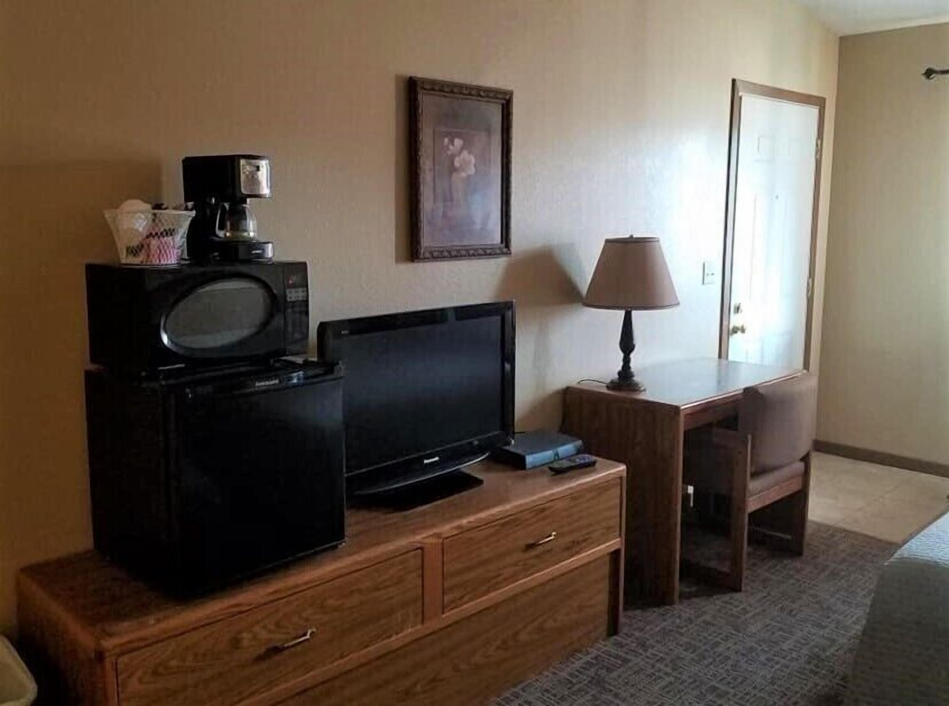 Una habitación de hotel con un escritorio de madera, televisión, lámpara y un cuadro en la pared.