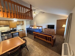 A compact hotel room with a kitchenette, a bed, a TV, a dresser, and a staircase.