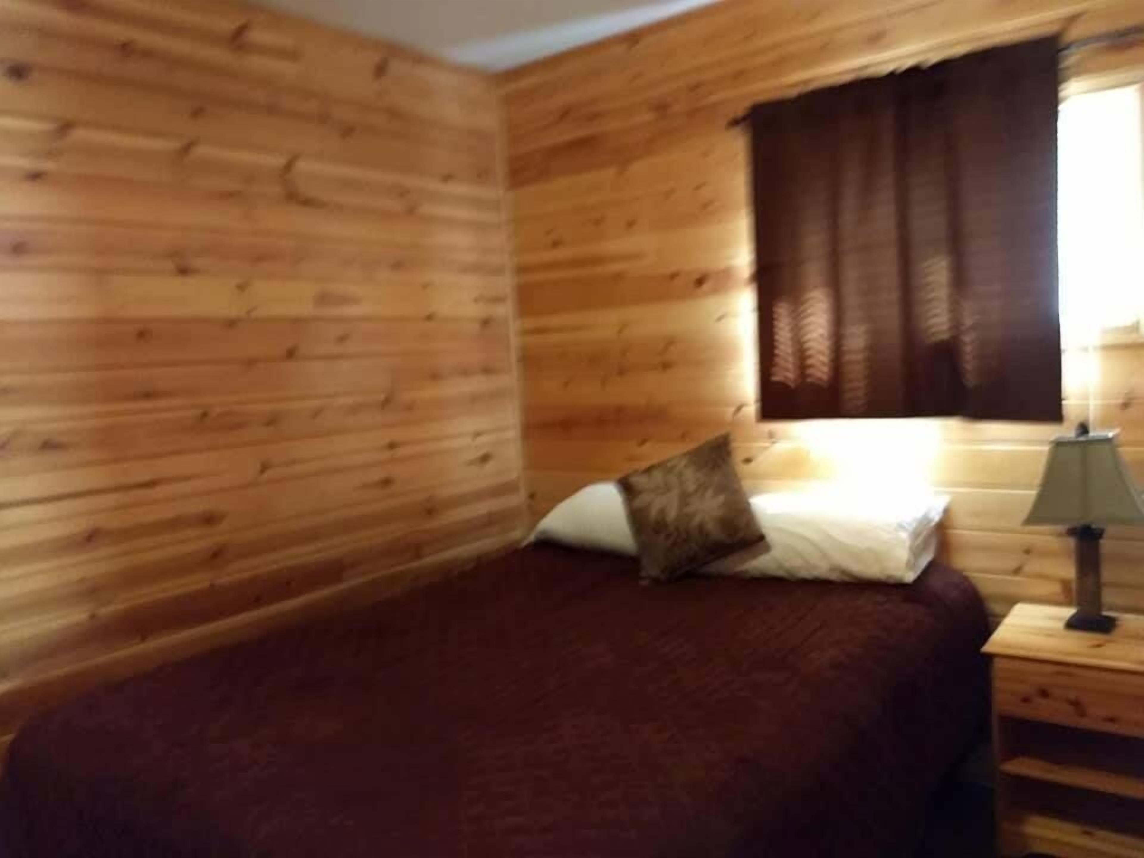 Una camera da letto in una baita di legno, con un letto, un comodino e una finestra con tende.