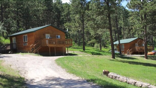 A wooden cabin with a balcony, surrounded by trees and a dirt path.