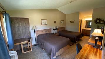 A hotel room with two beds, a desk, a chair, a lamp, and a radiator.