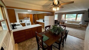 A kitchen with wooden cabinets, a central island, a dining table with chairs, and a ceiling fan.
