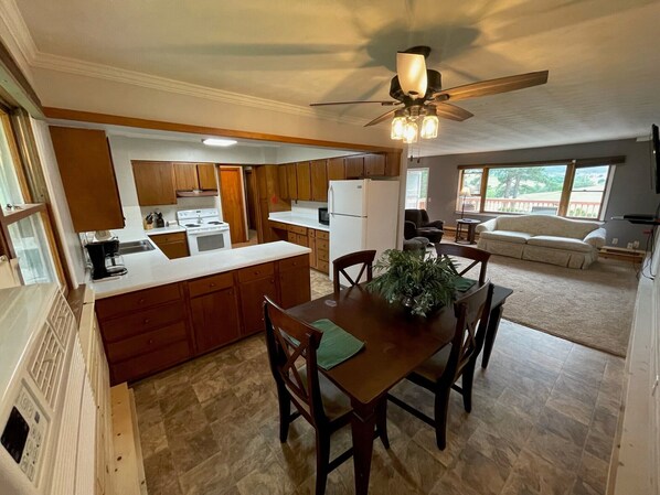 A kitchen with wooden cabinets, a central island, a dining table with chairs, and a ceiling fan.