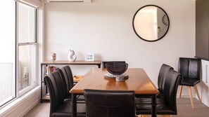 A dining area with a wooden table, black leather chairs, a round mirror on the wall, and a bookshelf in the background.