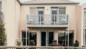 A two-story building with a balcony, large windows, and a door leading to an outdoor seating area. - Moyne Views 2 - Overlooking The Edge Of The Moyne River (Port Fairy)