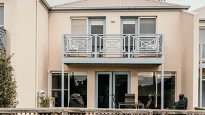 A two-story building with a balcony, large windows, and a door leading to an outdoor seating area. - Moyne Views 2 - Overlooking The Edge Of The Moyne River (Port Fairy)