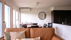 A living room with a sofa, a dining table, and a kitchen area with cabinets. - Moyne Views 2 - Overlooking The Edge Of The Moyne River (Port Fairy)