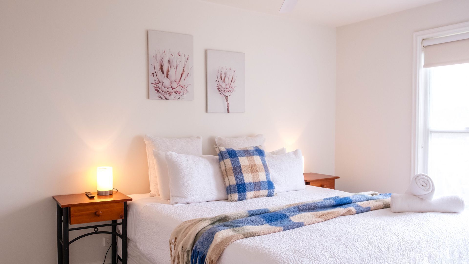 Un dormitorio con cama, mesitas de noche, lámpara, una obra de arte en la pared y una ventana.