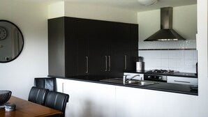 A modern kitchen with black cabinets, a stainless steel sink, and a gas stove. - Moyne Views 2 - Overlooking The Edge Of The Moyne River (Port Fairy)
