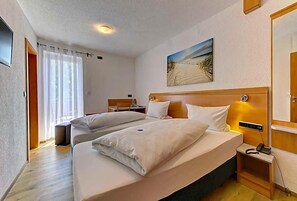 Une chambre d’hôtel avec deux lits, un tableau au mur, une table de chevet avec une lampe et une fenêtre avec des rideaux.