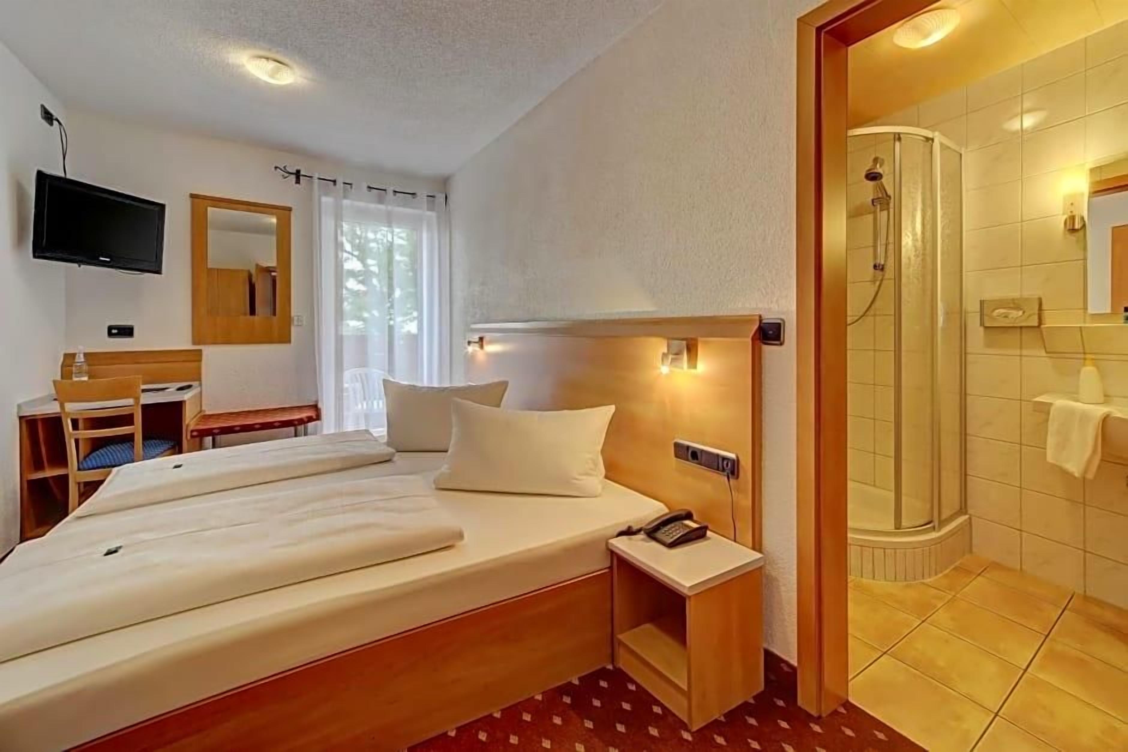 Une chambre d’hôtel comprenant un lit, une table de chevet, une télévision, un bureau, une chaise et un espace douche.