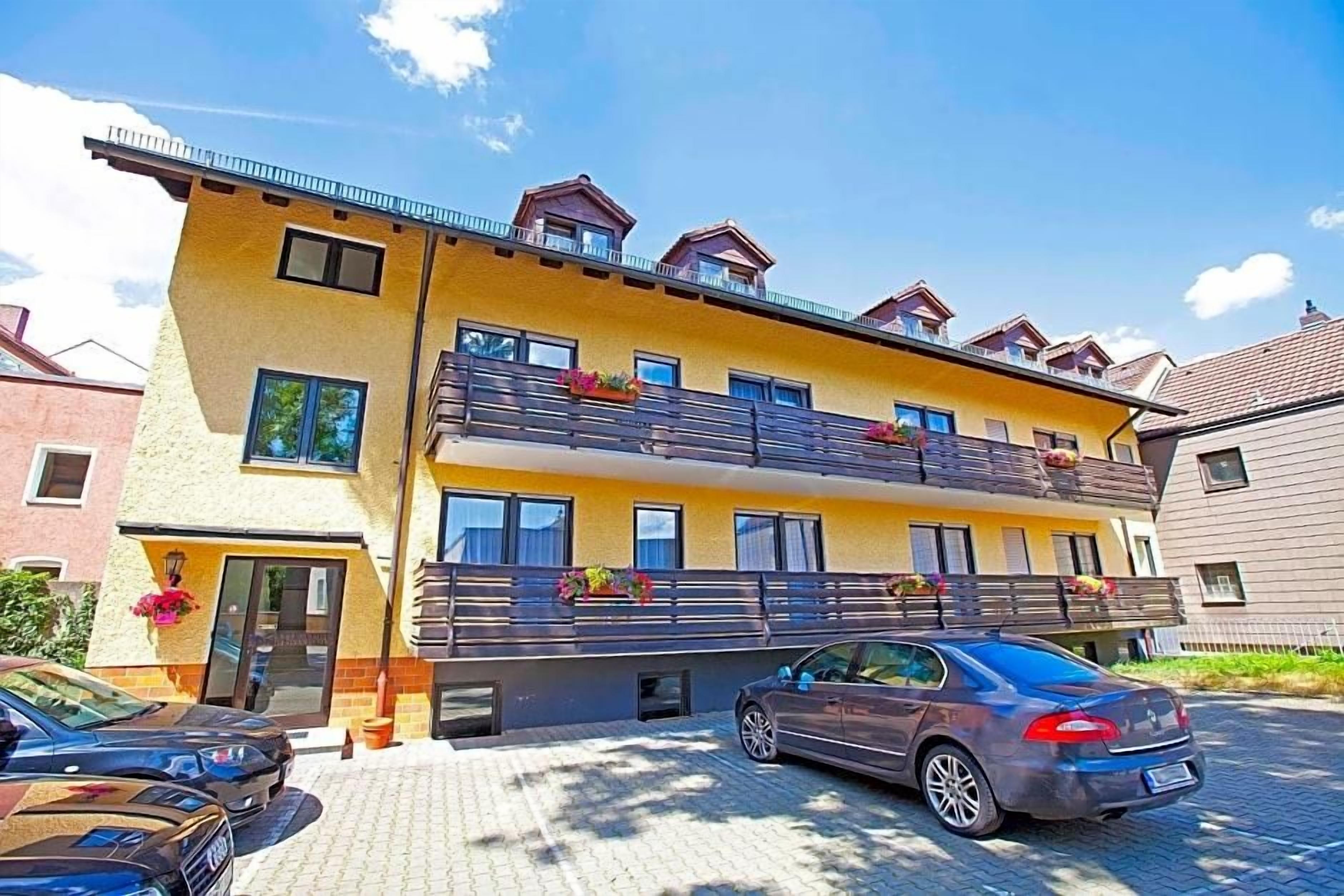 A multi-story building with balconies, a car parked in front, and a clear sky.