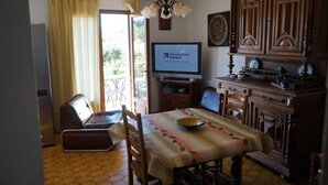 A living room with a sofa, a dining table with a bowl, a television displaying 'Boursorama Banque', and wooden cabinets. - Sunny A/C apartment with terrace overlooking countryside and private pool (Saint-Pargoire)