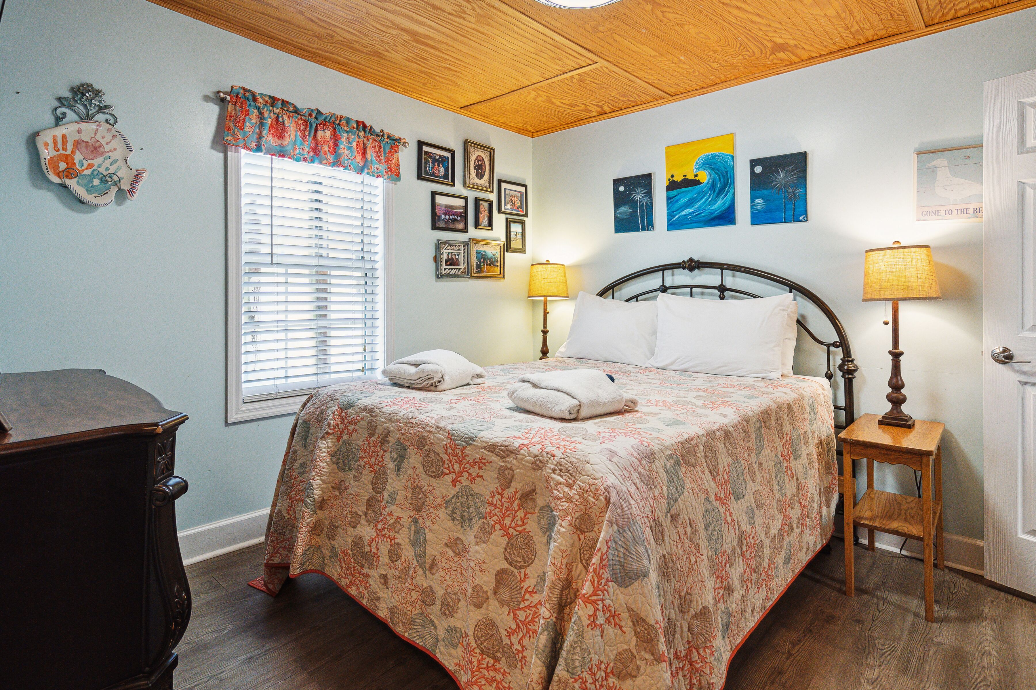 A bedroom with a bed, bedside lamps, a dresser, and a window with blinds.