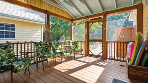 Eine überdachte Veranda mit Holzboden, grünen gepolsterten Stühlen, einem kleinen Tisch und einem Holzzaun.