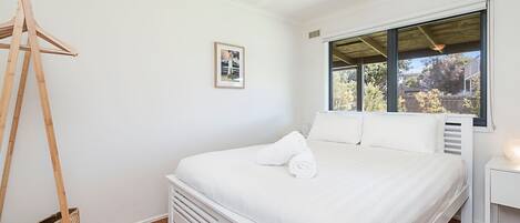 A bedroom with a bed, a wooden hanger, a framed picture, and a window with a view of trees and a building.
