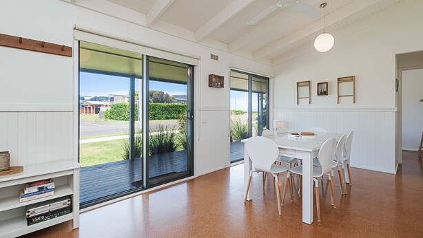 A modern dining area with a white table and chairs, large sliding glass doors leading to a garden view, and a ceiling fan. - Ocean Spray Retreat - sitting just block from the Southern Ocean (Port Fairy)