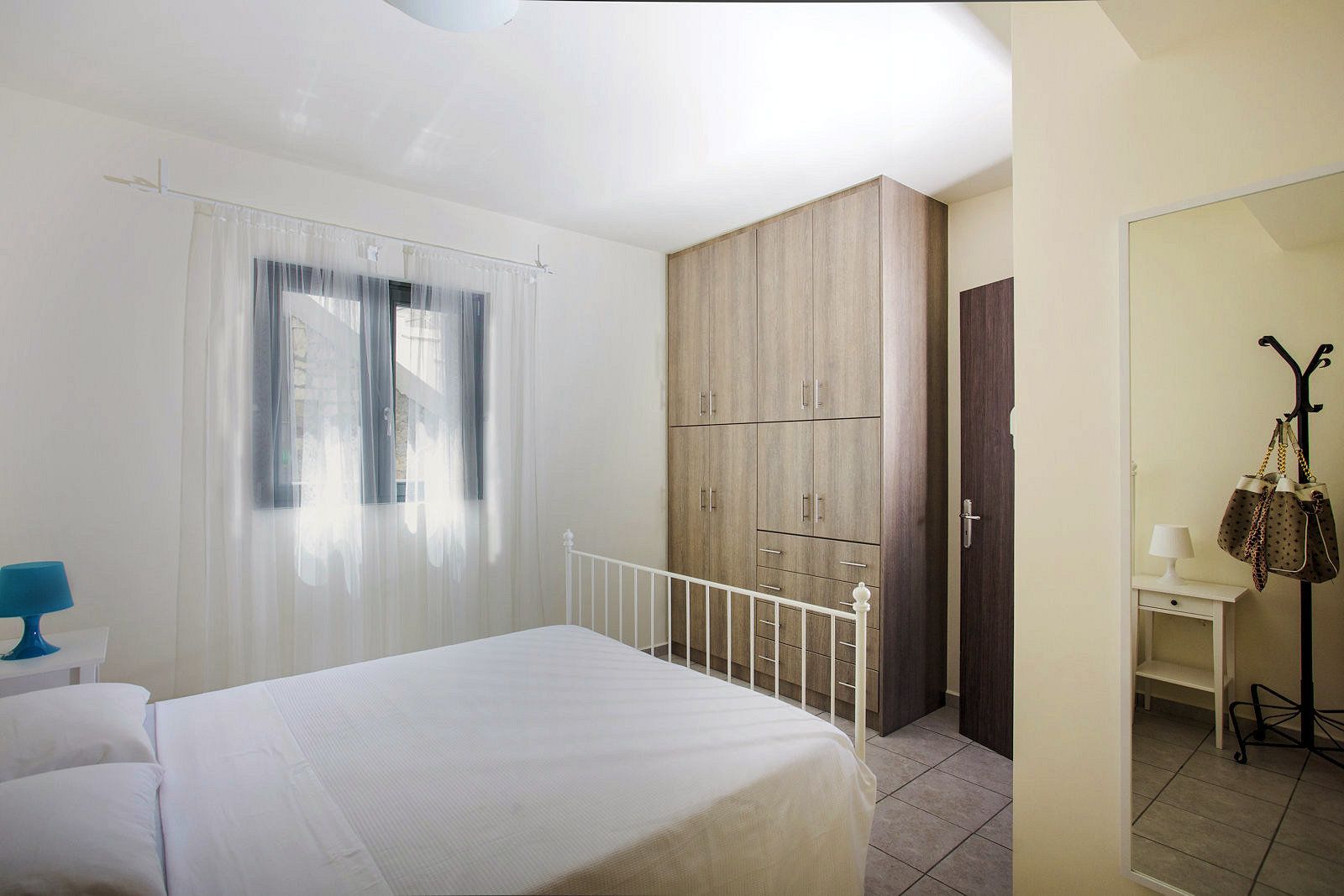 A bedroom with a bed, a wardrobe, a desk with a lamp, and a hanging bag.