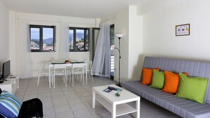 A modern living room with a grey sofa, colorful cushions, a dining table with chairs, a TV, and a floor lamp. - Ithaca's Poem (Ithaki)