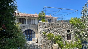 Un edificio de piedra con techo de tejas, una ventana pequeña y una puerta. Hay una cesta grande de mimbre en el suelo y una estructura metálica encima.