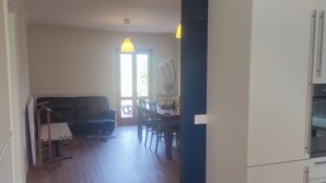 Eine moderne Küche mit weißen Schränken und einem eingebauten Ofen. Es gibt einen Essbereich mit Tisch und Stühlen, und eine Couch im Hintergrund.
