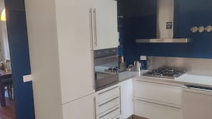 A modern kitchen with white cabinets, a built-in oven, a gas stove, and a stainless steel range hood.