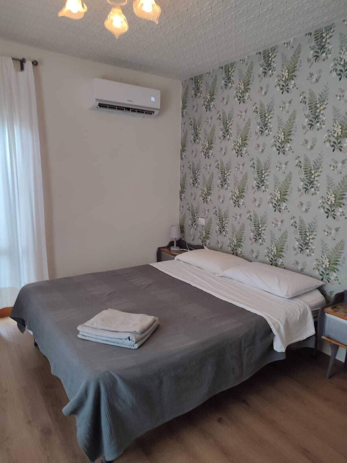 Una camera da letto con un letto, un comodino, un condizionatore d'aria e carta da parati con motivi floreali.