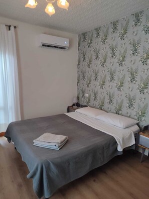 Ein Schlafzimmer mit Bett, Nachttisch, Klimaanlage und floralem Wandpapier.