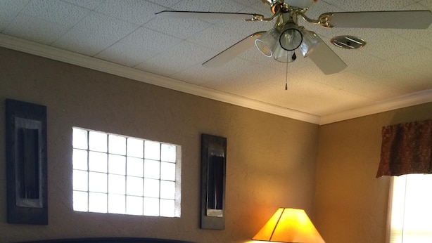Une chambre à coucher avec un lit, un ventilateur de plafond, une fenêtre et une lampe.