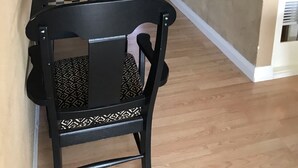 Un couloir doté d’un plancher en bois, d’une chaise noire avec un coussin à motifs et d’une table dont le plateau est à carreaux.