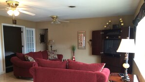 Un salon avec deux canapés rouges, un ventilateur de plafond, un meuble en bois et une lampe.